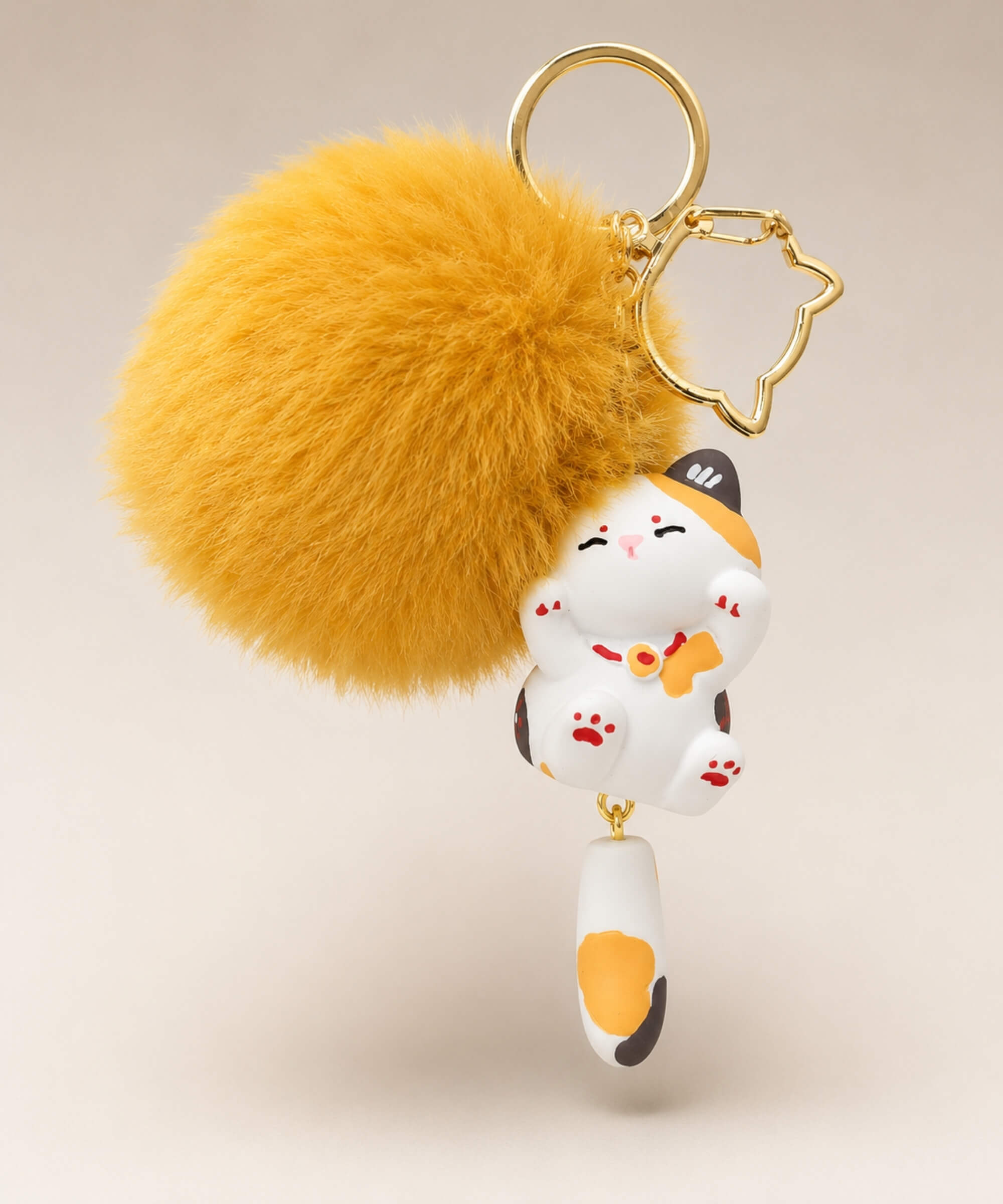Calico cat pom pom resin keychain with fluffy plush ball and gold hardware on a neutral background
